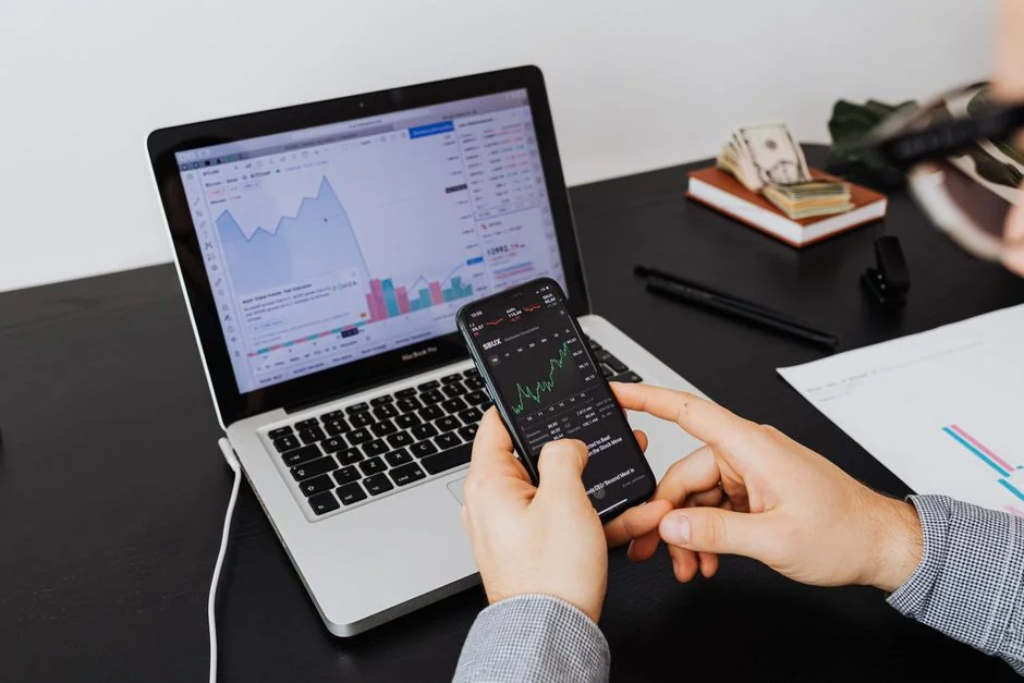 Personne utilisant un smartphone pour analyser le marché boursier dans un bureau à domicile.